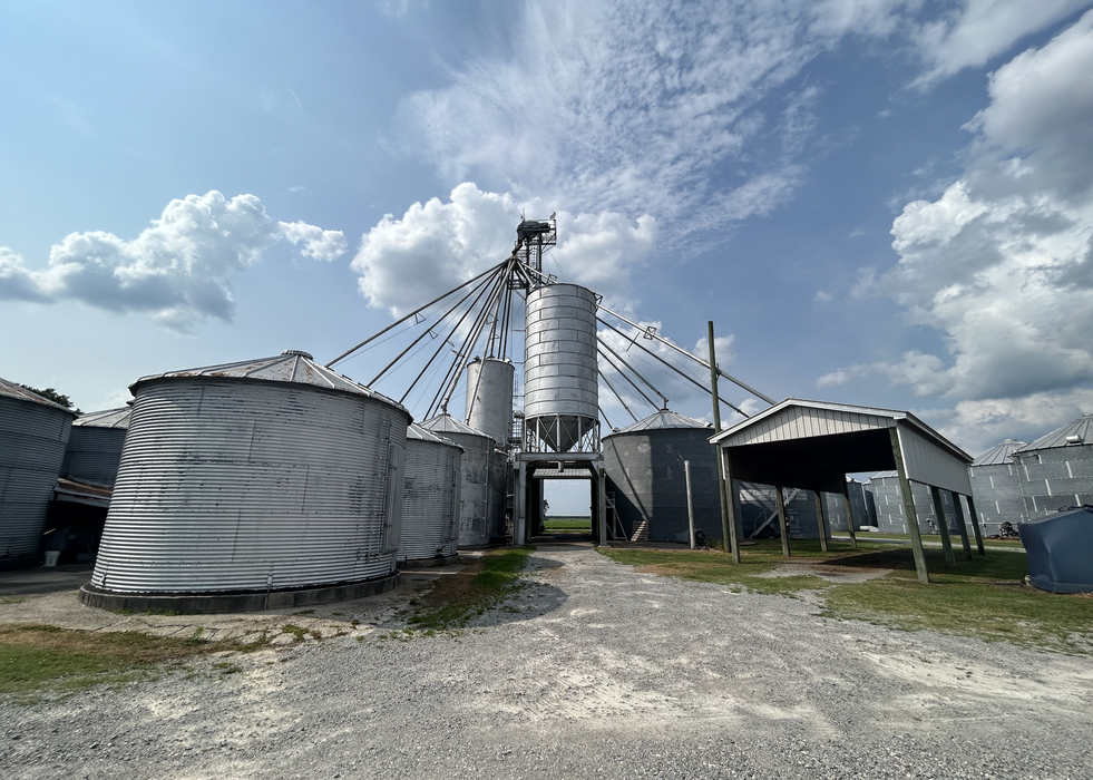 Large metal grain silos with connecting conveyors under a partly cloudy sky