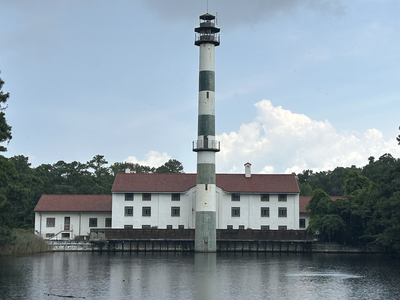 Tall green-and-white striped lighthouse rising from center of white building by a lake