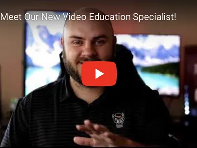 Man in dark polo gesturing toward camera with text "Meet Our New Video Education Specialist!"
