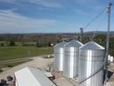 Three large metal grain silos with conveyor towers on a rural farm