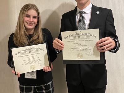 two teens in professional clothing hold award certificates