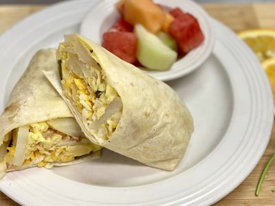 Breakfast burrito cut in half on a white plate with a small bowl of mixed fruit