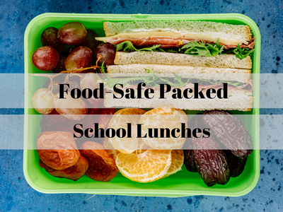 Green lunchbox with sandwich, grapes, orange slices and dried fruit; text: "Food-Safe Packed School Lunches"