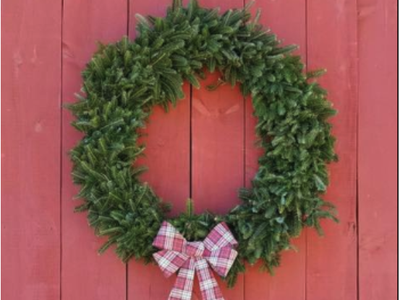 Green evergreen wreath with red-and-white plaid bow on red wooden door