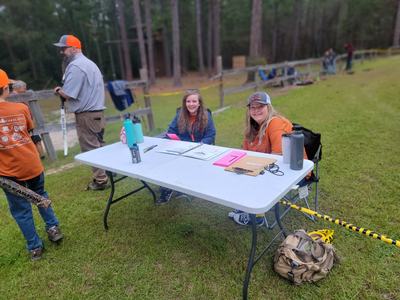 Two women seated at an outdoor registration table with clipboards and water bottles