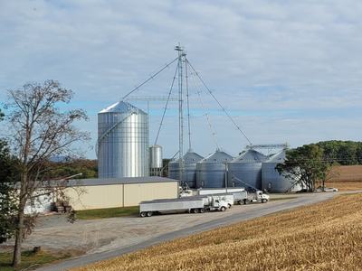 Grain elevators and metal silos with trucks parked at a rural farm facility