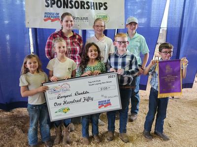 children pose with giant check award by poultry show banner