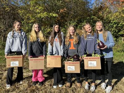 Six girls outdoors holding boxes labeled "KEEP REFRIGERATED" filled with eggplants