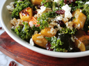 Bowl of kale salad with roasted squash, brown rice, dried cranberries, feta, and pumpkin seeds
