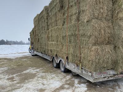 Trailer loaded with stacked hay bales secured by straps on snowy ground