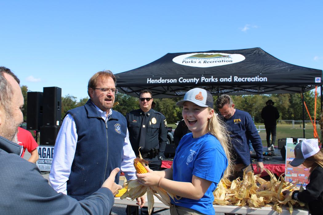 Adults speak with a girl shucking corn.