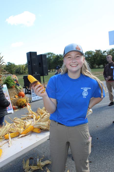 A girl holds a cob of corn.