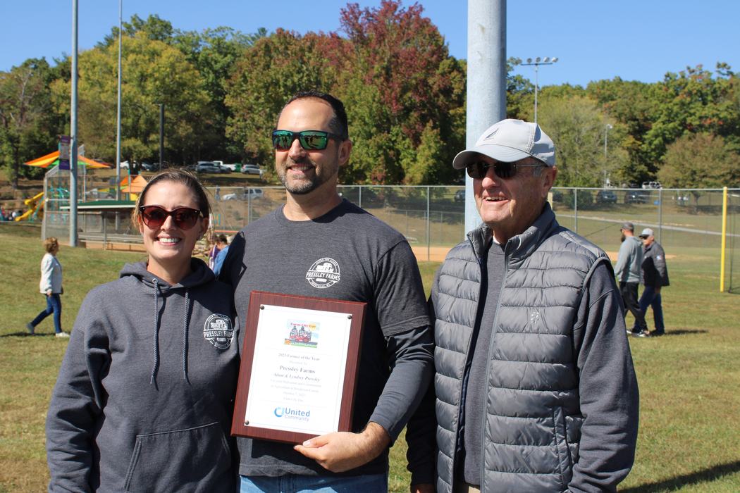 Three people pose with a plaque. 