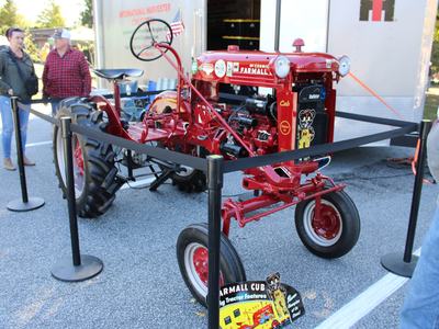 Red McCormick Farmall Cub tractor on display behind stanchions, sign "FARMALL CUB"