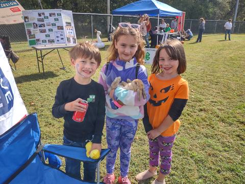 Three children at outdoor fair, middle child holding a brown rabbit