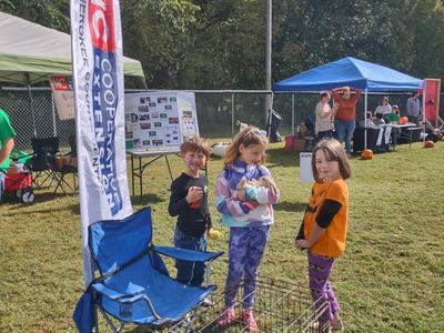 Three children at an outdoor booth, one holding a small rabbit; banner reads "NC Cooperative Extension"