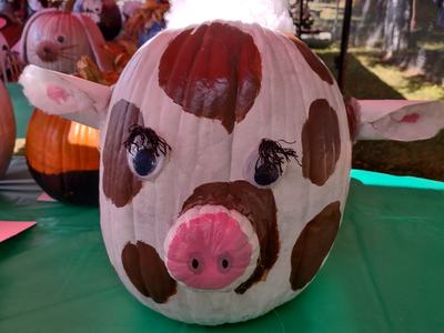 Pumpkin painted as a spotted pig with pink snout and cotton tuft on top, on green table
