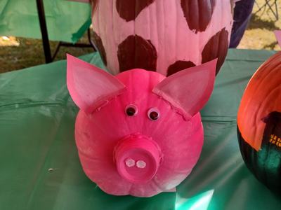 Painted pink pumpkin made into pig with bottle snout and googly eyes on green table
