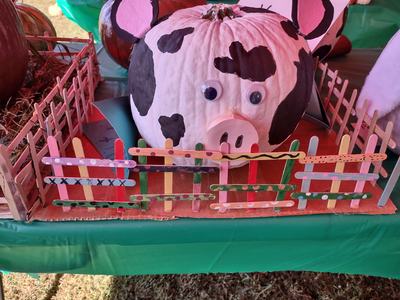 White pumpkin painted like a cow with googly eyes behind a colorful popsicle-stick fence