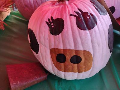 White pumpkin painted like a cow with black spots and a brown snout on a green table
