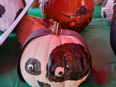 White pumpkin painted with black panda face and googly eyes on green table