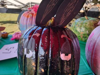 Painted dark pumpkin with painted eyes and two large black bunny ears on a green table