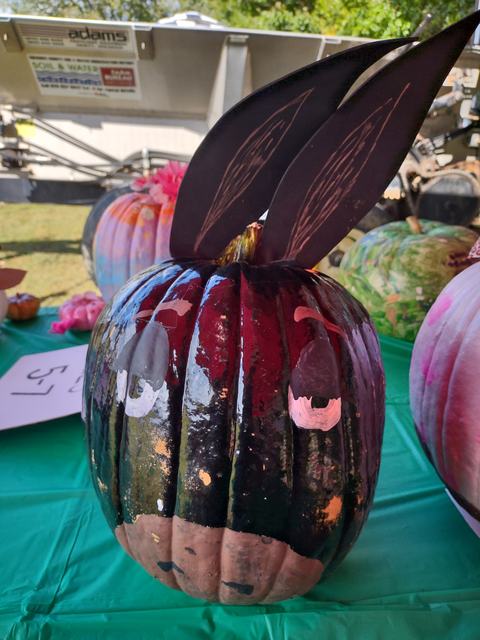 Painted dark pumpkin with painted eyes and two large black bunny ears on a green table