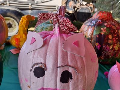 Pink pumpkin decorated as a pig with paper ears, painted snout and black eyes, leopard bow