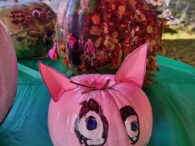 Pink painted pumpkin with paper ears and painted eyes and snout on a green table