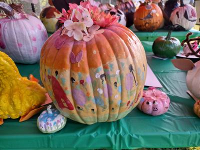 Large painted pumpkin with flower topper and glitter butterflies on green table
