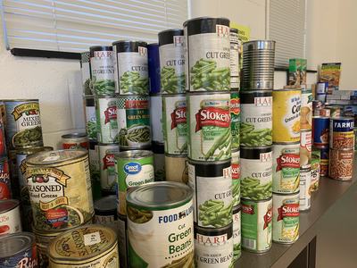 Stacks of canned goods on a table, mainly labeled "Cut Green Beans" and mixed vegetables