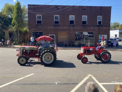 Two vintage tractors driving past a brick storefront during a street parade