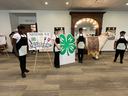 Nash County 4-H Carolina Choppers wear aprons and pose by challenge sign and 4-H clover logo