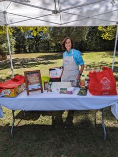 Person standing behind vendor table under canopy with brochures, bags, and display