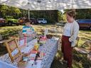 Child standing behind outdoor vendor table with displayed items; adult standing opposite.