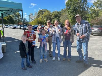 Seven people outdoors holding award ribbons and small prizes in a parking lot