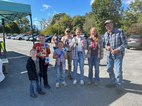 Seven people outdoors holding award ribbons and small prizes in a parking lot