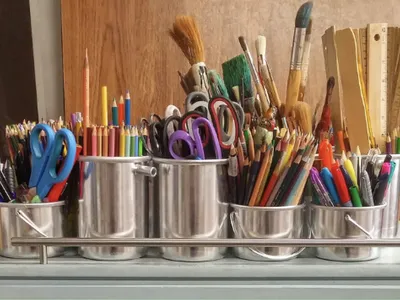Open book with glasses; metal cups holding pencils, brushes and scissors; girl in lab coat observing green solution