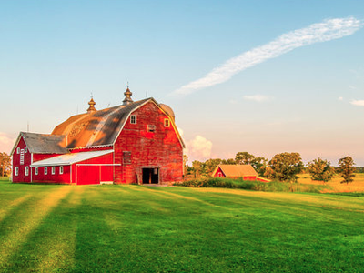 Large red barn on green field at sunrise with smaller outbuilding and trees