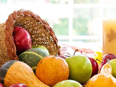 Wicker cornucopia on table spilling apples, gourds, candles, and a sunflower