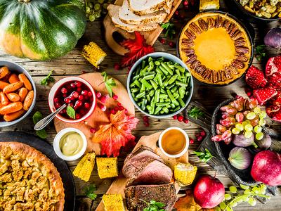 table spread with fall foods, pies, fruits, ham, squash, cranberries, corn