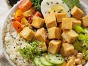 Bowl of rice topped with cubed tofu, cucumber, cherry tomatoes, half boiled egg, chickpeas