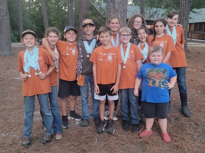 Kids wearing orange "Henderson County" shirts and medals standing outdoors by trees