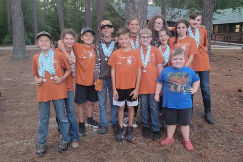Kids wearing orange "Henderson County" shirts and medals standing outdoors by trees