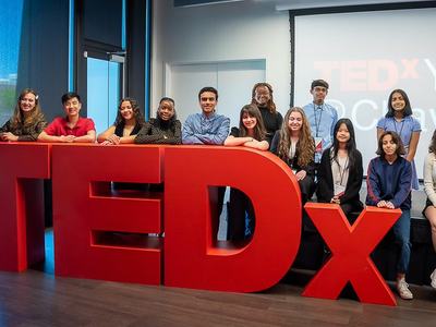 Youth gather around TEDx letters.