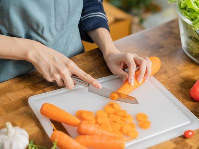 Hands slicing carrots on white cutting board with bowl of lettuce nearby