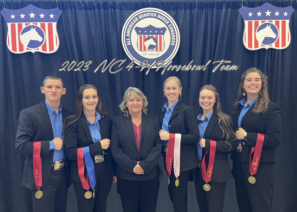 Six people in blazers wearing medals under sign reading "2023 NC 4-H Horsebowl Team"