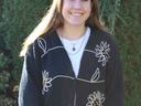 Person smiling, wearing black cardigan with white flower designs, standing outdoors