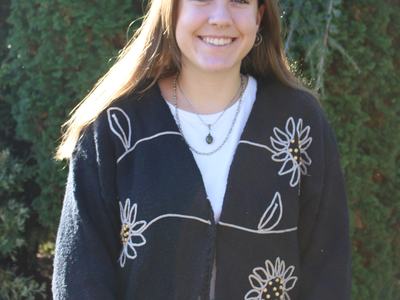 Person smiling, wearing black cardigan with white flower designs, standing outdoors