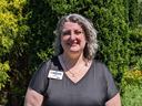 Woman standing in front of evergreen shrubs, black shirt, badge reading "NC Cooperative Extension"